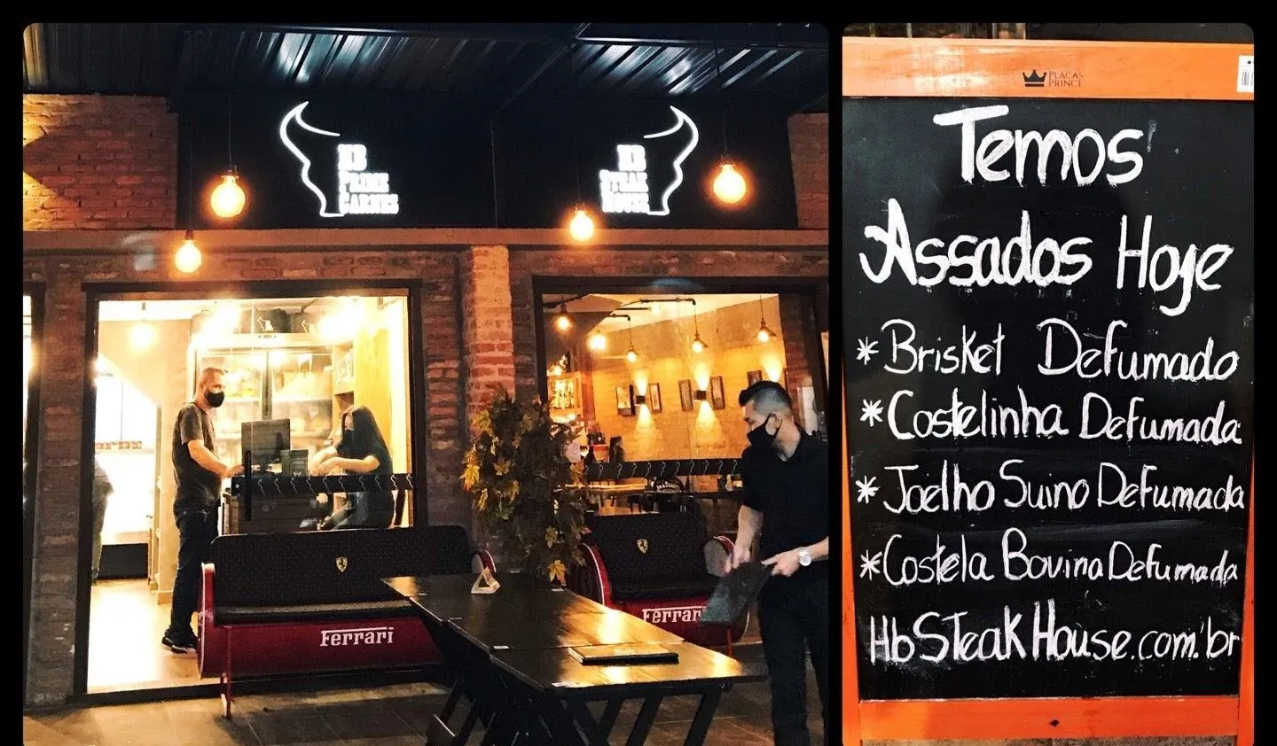 Entrada da HB à noite, com a lousa listando brisket, costelinha, joelho suíno e costela bovina defumados